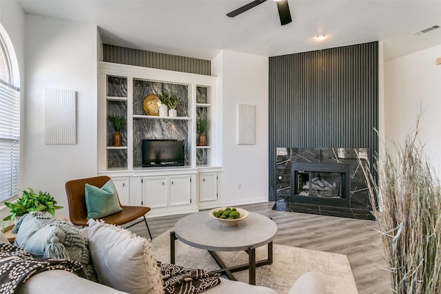 living room featuring light wood-style floors, a high end fireplace, visible vents, and ceiling fan