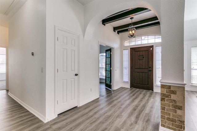 entryway with beam ceiling, a chandelier, a wealth of natural light, and wood finished floors