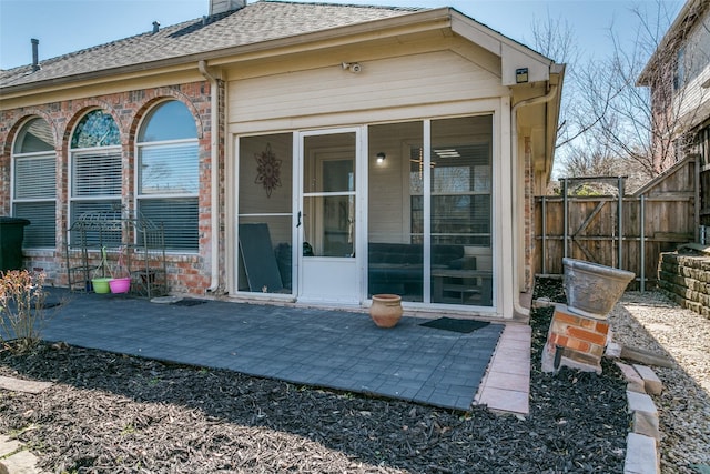 rear view of house with a patio, a sunroom, a chimney, roof with shingles, and fence