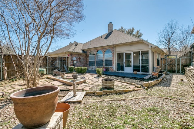 rear view of property with an outdoor fire pit, a fenced backyard, brick siding, a chimney, and a patio area