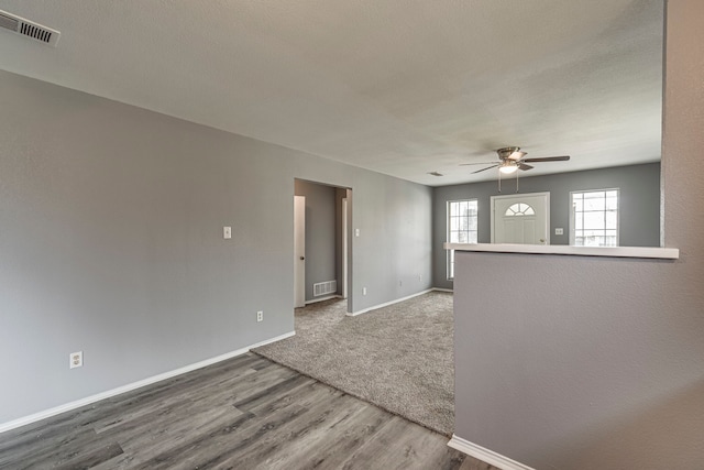 empty room featuring ceiling fan, wood finished floors, visible vents, and baseboards