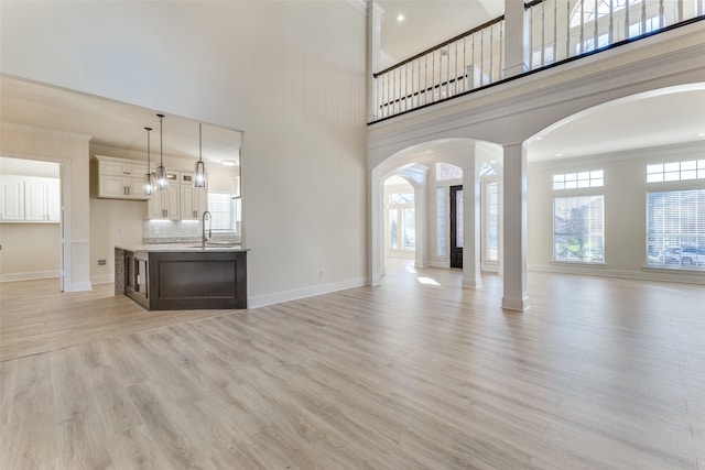 unfurnished living room with baseboards, arched walkways, a towering ceiling, light wood-style floors, and a sink