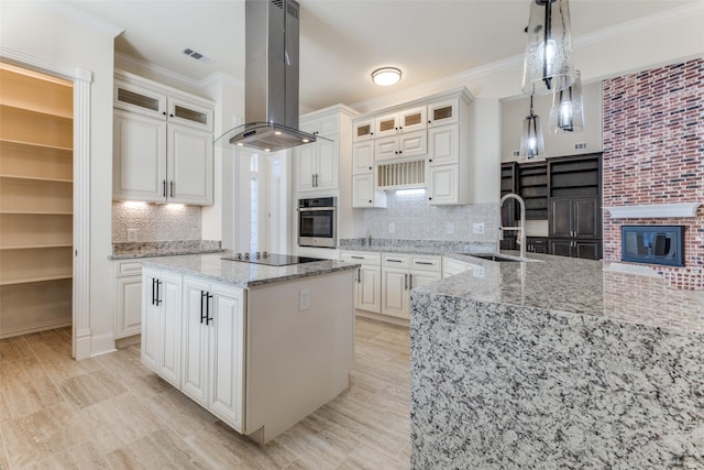 kitchen featuring visible vents, ornamental molding, oven, island exhaust hood, and a sink