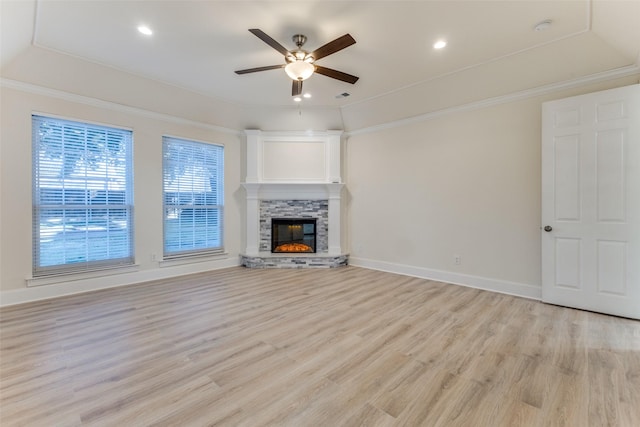 unfurnished living room featuring a raised ceiling, a ceiling fan, light wood-style flooring, ornamental molding, and a fireplace