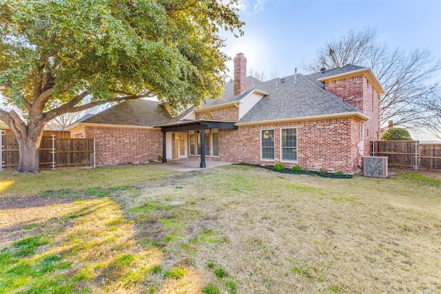 rear view of property with brick siding, a yard, a chimney, and fence