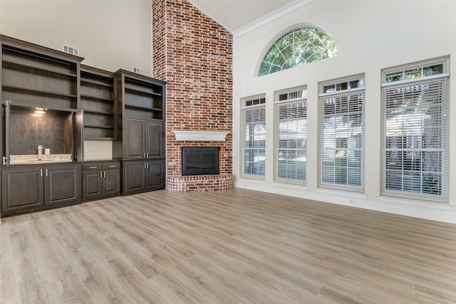 unfurnished living room featuring ornamental molding, light wood-style floors, a fireplace, high vaulted ceiling, and a sink