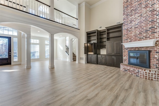 unfurnished living room featuring a fireplace, baseboards, light wood-type flooring, decorative columns, and crown molding