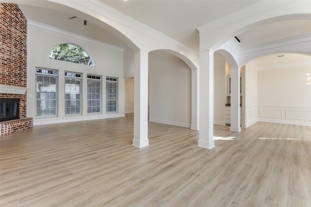 unfurnished living room with crown molding, light wood finished floors, a decorative wall, a high ceiling, and a brick fireplace