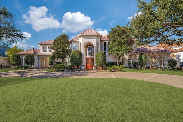 mediterranean / spanish-style house with stucco siding, driveway, a tile roof, french doors, and a front yard