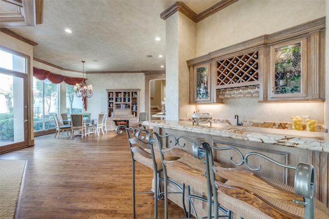 kitchen featuring glass insert cabinets, ornamental molding, light stone counters, recessed lighting, and wood finished floors