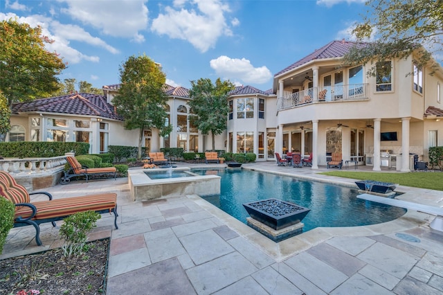 view of pool featuring a patio, exterior kitchen, a diving board, a pool with connected hot tub, and ceiling fan