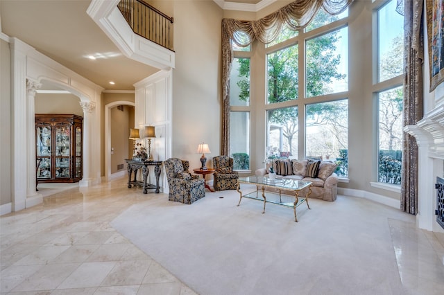 living area featuring baseboards, ornate columns, a high ceiling, a fireplace with flush hearth, and arched walkways