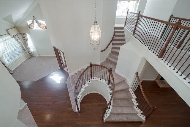 staircase featuring a towering ceiling, baseboards, and wood finished floors