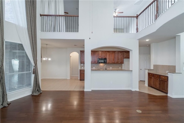 unfurnished living room with light wood-type flooring, baseboards, arched walkways, and a ceiling fan