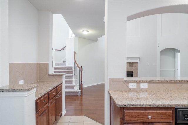 kitchen featuring light stone counters, brown cabinets, a fireplace, backsplash, and light tile patterned flooring