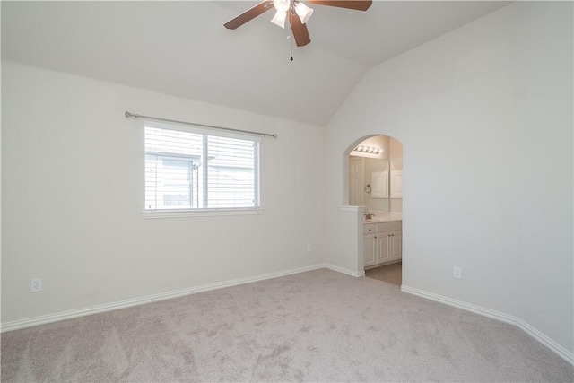 unfurnished bedroom with arched walkways, lofted ceiling, ensuite bathroom, light carpet, and baseboards