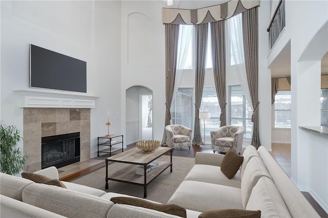 tiled living area with a high ceiling, baseboards, arched walkways, and a tiled fireplace