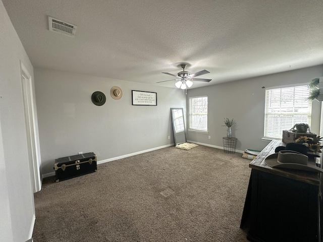 interior space featuring visible vents, dark carpet, ceiling fan, a textured ceiling, and baseboards