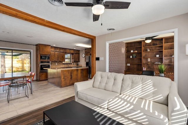 living area featuring light wood finished floors, beam ceiling, visible vents, and a ceiling fan