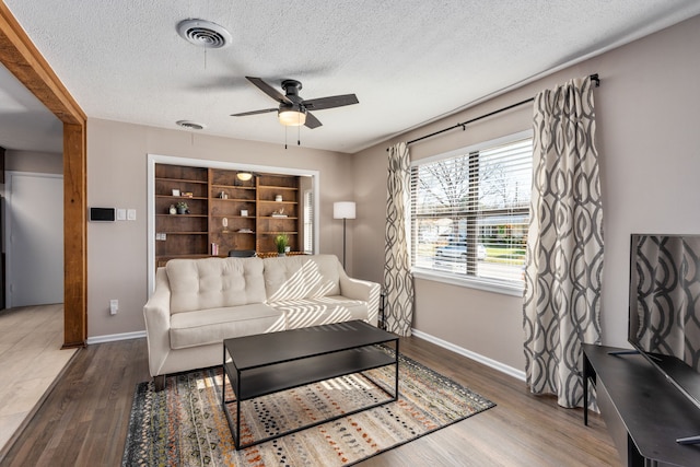 living area featuring visible vents, ceiling fan, baseboards, and wood finished floors