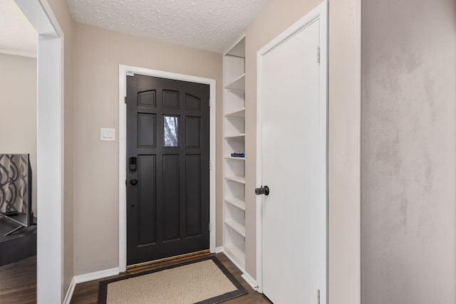 foyer with dark wood finished floors, a textured ceiling, and baseboards