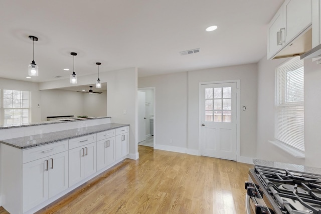 kitchen with decorative light fixtures, visible vents, light wood-style flooring, gas stove, and white cabinetry