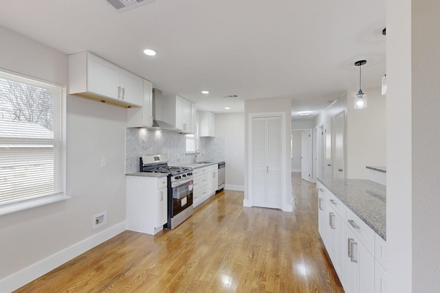 kitchen with wall chimney exhaust hood, appliances with stainless steel finishes, a sink, light wood-type flooring, and backsplash