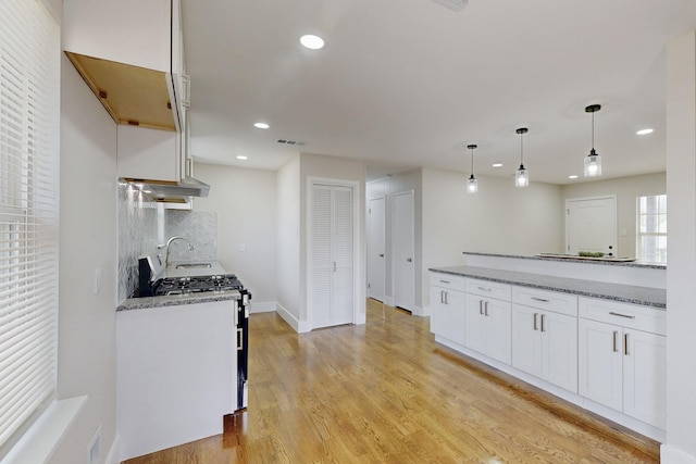 kitchen with stainless steel gas stove, light wood-style flooring, white cabinetry, and light stone counters