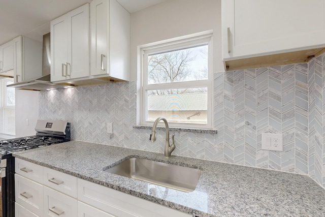 kitchen featuring stainless steel range with gas cooktop, decorative backsplash, white cabinets, a sink, and wall chimney exhaust hood