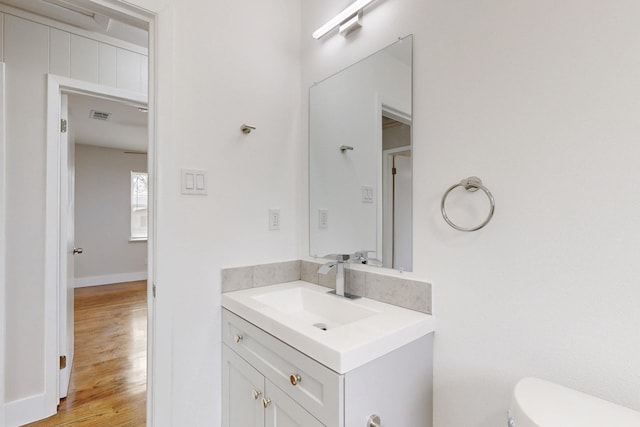 half bathroom with visible vents, vanity, toilet, and wood finished floors