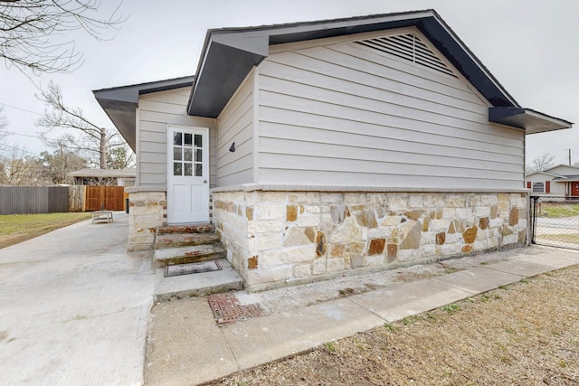 exterior space featuring entry steps, stone siding, and fence