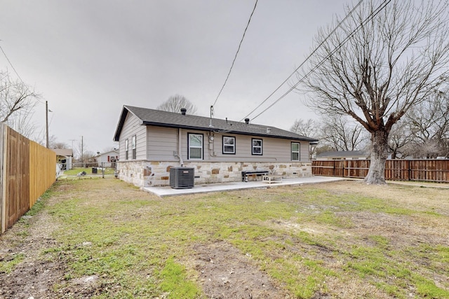 rear view of house featuring a patio, stone siding, a fenced backyard, cooling unit, and a yard