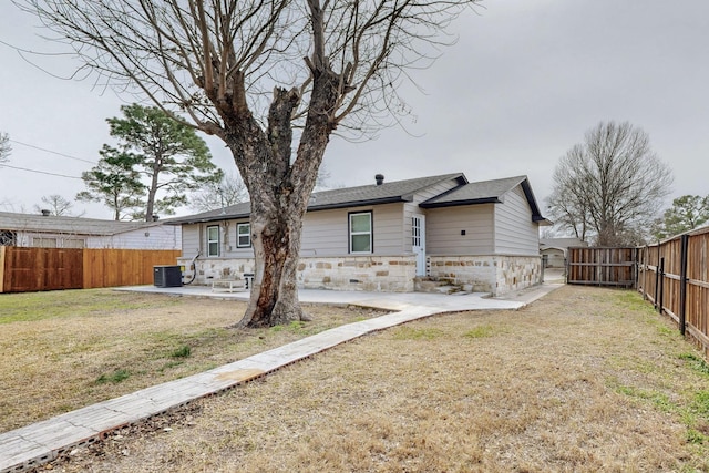 back of house featuring a patio, a fenced backyard, stone siding, a lawn, and a gate