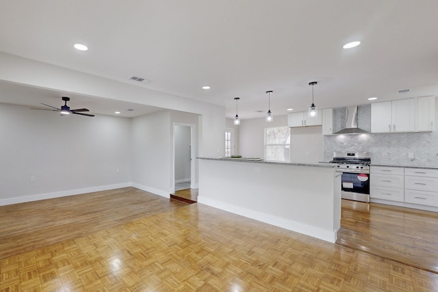 kitchen featuring white cabinetry, wall chimney range hood, stainless steel gas range oven, and visible vents