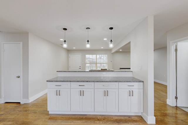 kitchen with decorative light fixtures, white cabinetry, light stone countertops, light wood-type flooring, and baseboards