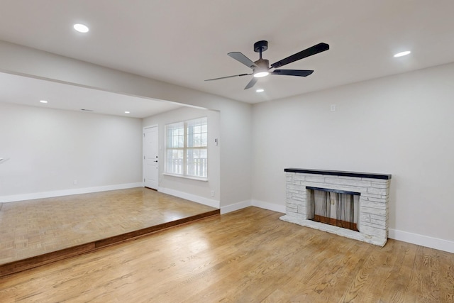 unfurnished living room featuring recessed lighting, a stone fireplace, baseboards, and wood finished floors