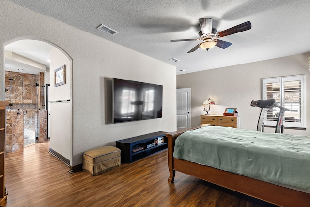 bedroom featuring arched walkways, visible vents, a textured wall, a textured ceiling, and wood finished floors