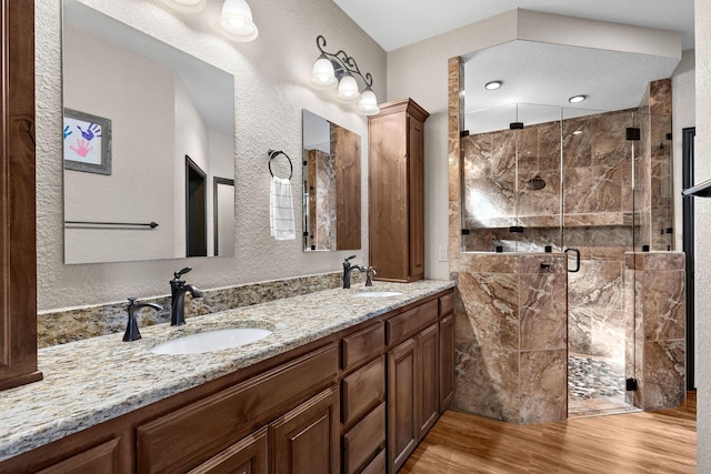 full bath with double vanity, a stall shower, a sink, and wood finished floors