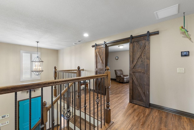 hall with a barn door, wood finished floors, an inviting chandelier, a textured ceiling, and an upstairs landing