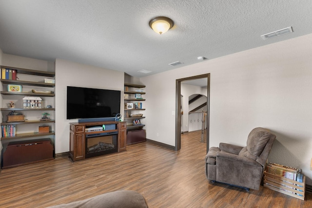 living room featuring a textured ceiling, wood finished floors, visible vents, and baseboards