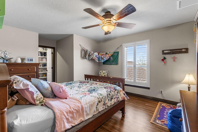 bedroom with a textured ceiling, a textured wall, wood finished floors, visible vents, and baseboards