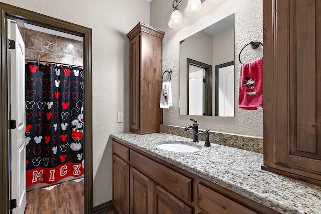 full bathroom with a textured wall, curtained shower, wood finished floors, and vanity