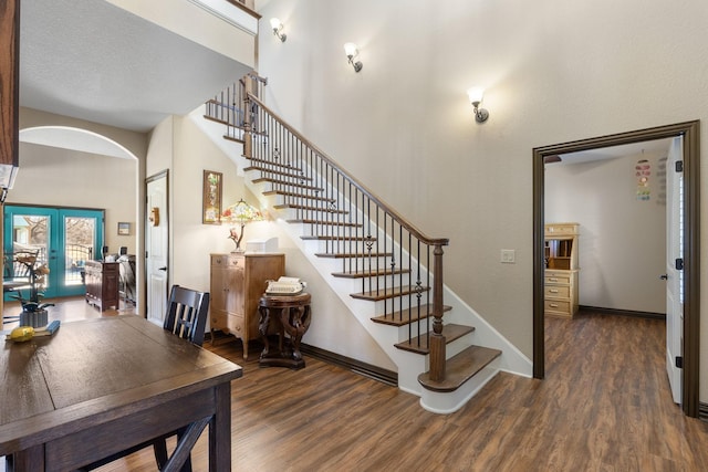 stairway featuring baseboards, arched walkways, wood finished floors, and french doors