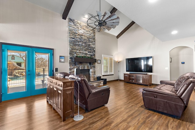 living area featuring arched walkways, wood finished floors, a fireplace, high vaulted ceiling, and beam ceiling