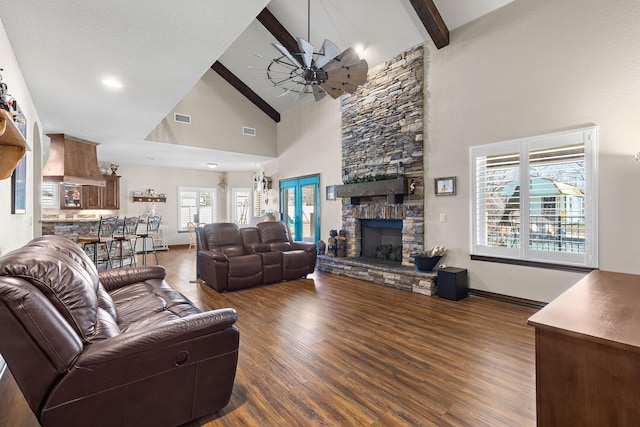 living room with visible vents, beamed ceiling, a stone fireplace, and wood finished floors