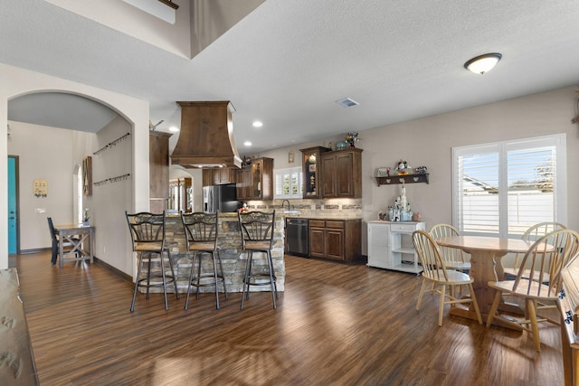 kitchen featuring arched walkways, dark brown cabinetry, dark wood-style flooring, stainless steel fridge with ice dispenser, and dishwasher