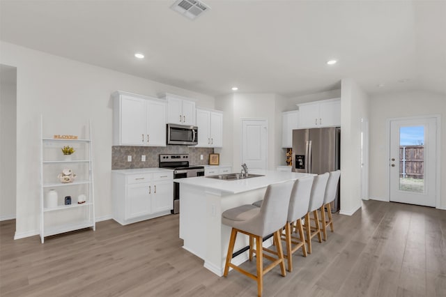 kitchen with stainless steel appliances, visible vents, backsplash, white cabinetry, and a kitchen bar