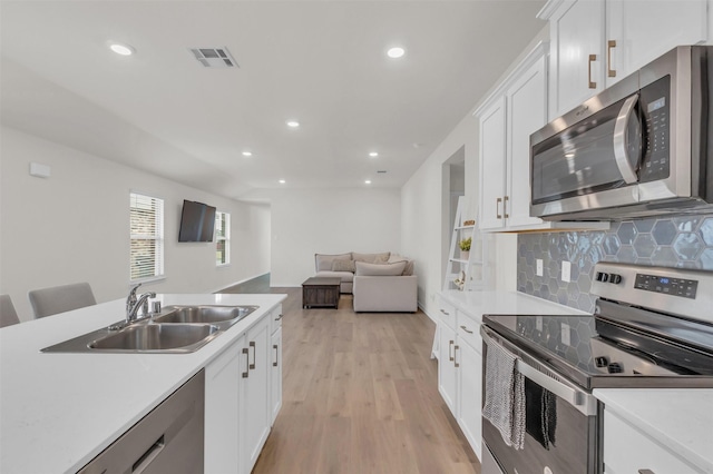 kitchen featuring visible vents, a sink, stainless steel appliances, white cabinetry, and backsplash