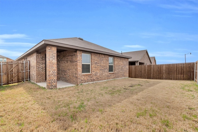 back of house with a yard, brick siding, a patio area, and a fenced backyard