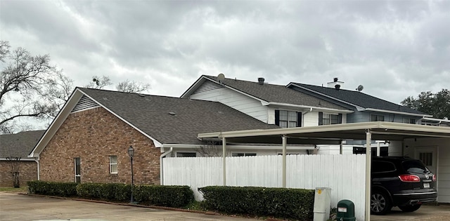 view of home's exterior with a carport, brick siding, a shingled roof, and fence